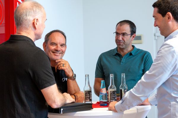Four people in technical discussion at a standing table in front of the IDT exhibition stand