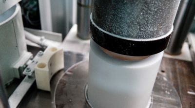 White cylindrical PTFE blank in a press, compacted from above by a metallic punch