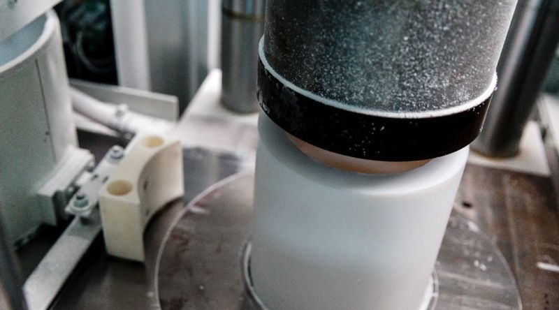 White cylindrical PTFE blank in a press, compacted from above by a metallic punch